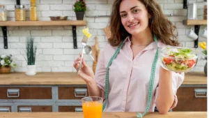 Mulher segurando uma tijela de vidro com verduras cortadas dentro com a mão esquerda e um garfo com uma verdura espetada na mão direita