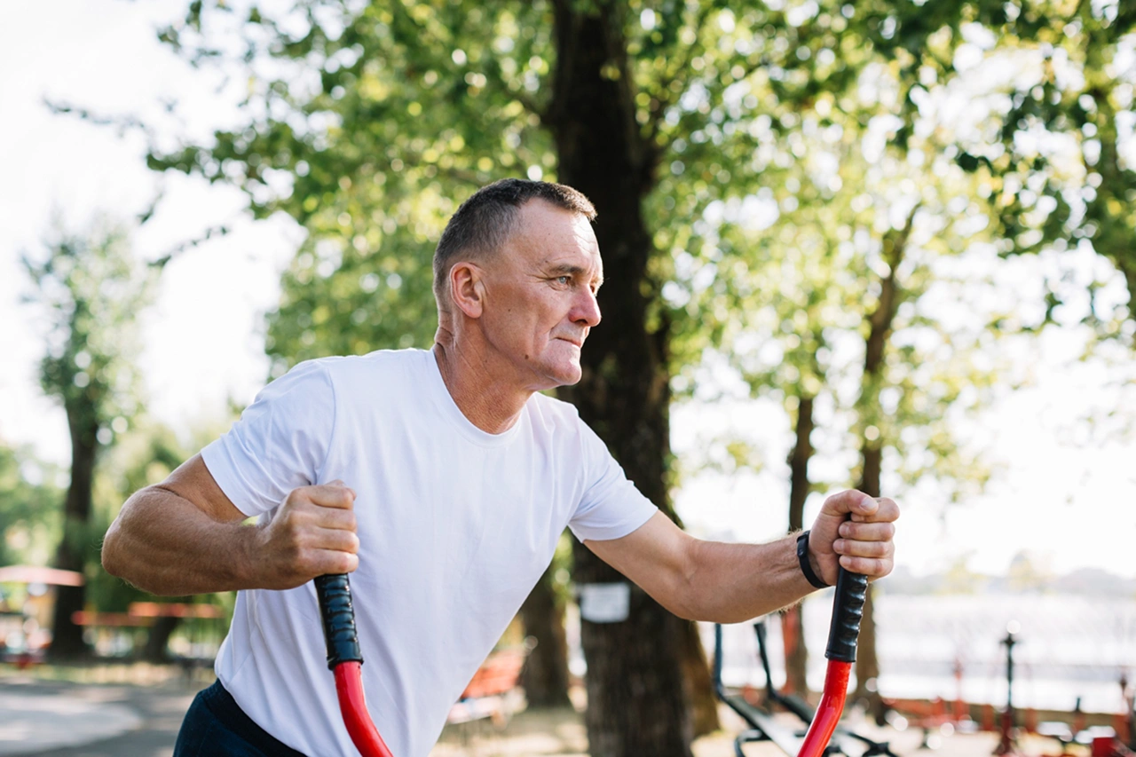Texto alternativo: Exercício físico após os 40 — homem de meia-idade a exercitar-se ao ar livre numa máquina de cardio, com foco em técnica e prevenção de lesões.