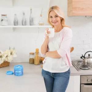 Mulher com um copo na mão e um produto para controle de peso em cima de uma bancada.